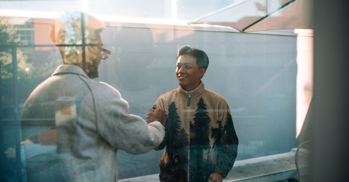Two men are shaking hands in front of a glass wall.