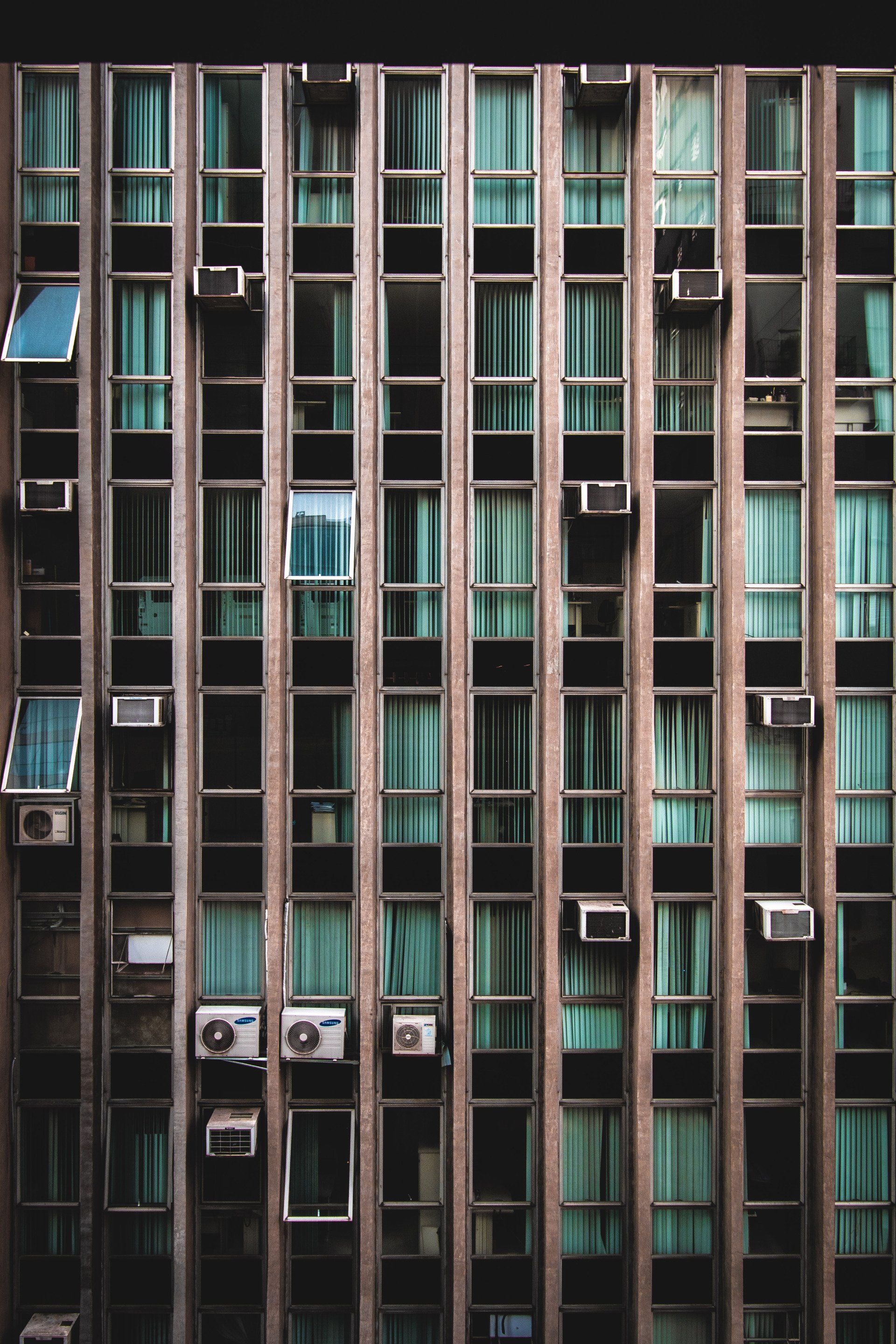 Tall apartment building facade with rows of teal curtains and many window air conditioners