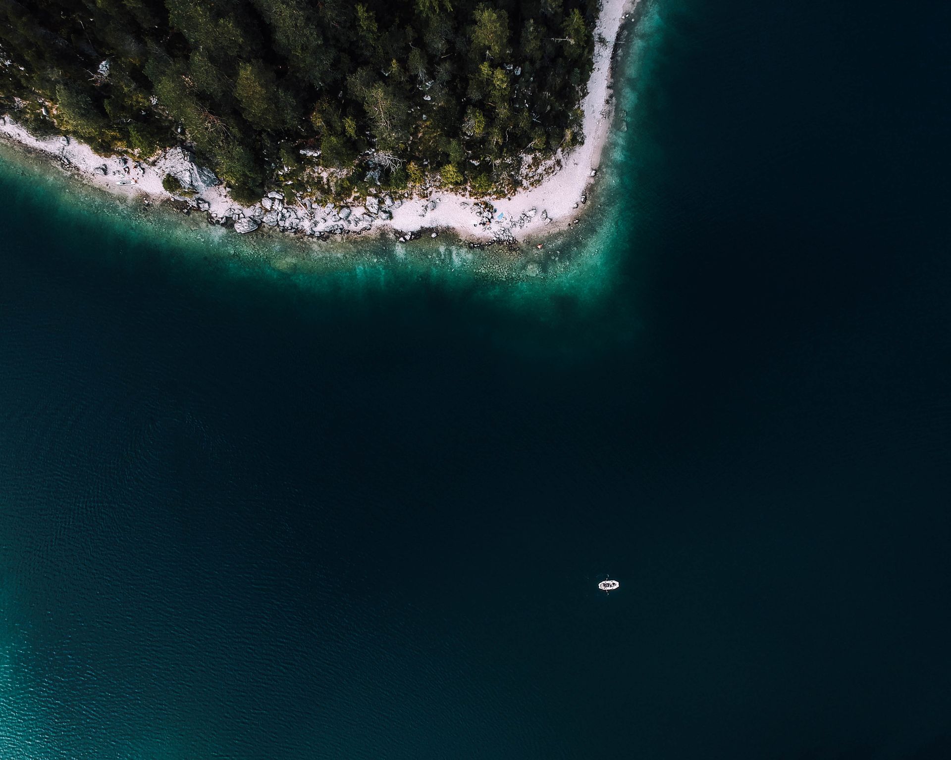 Aerial view of a forested peninsula bordering dark turquoise water; a small boat floats offshore.