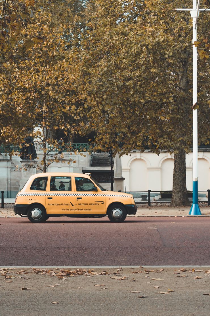 Yellow London taxi on a street, autumn trees in the background.