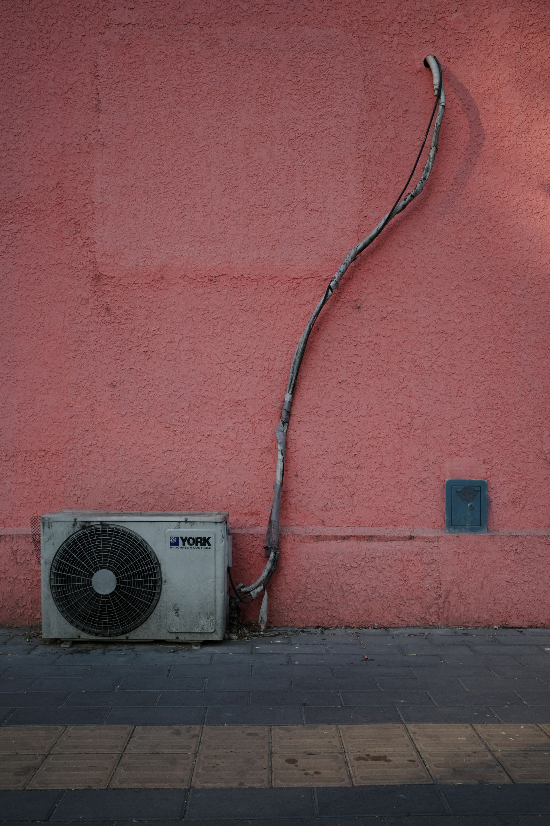 A white air conditioner is attached to a pink wall.
