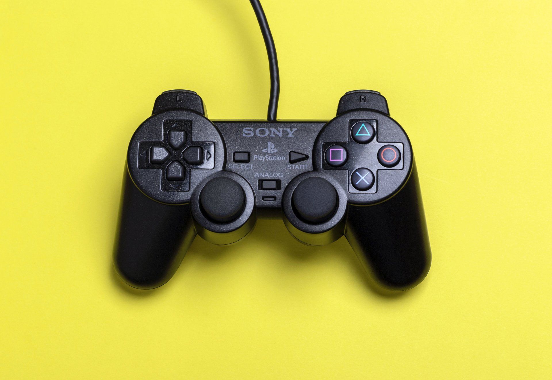 Black Sony PlayStation 2 controller on a yellow background.