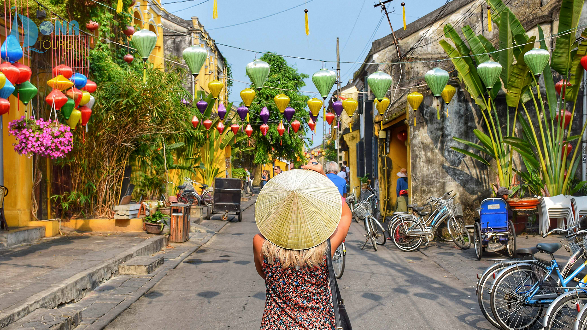 A woman is walking down a street holding a hat on her head.
