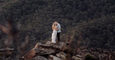 A bride and groom are kissing on top of a mountain.