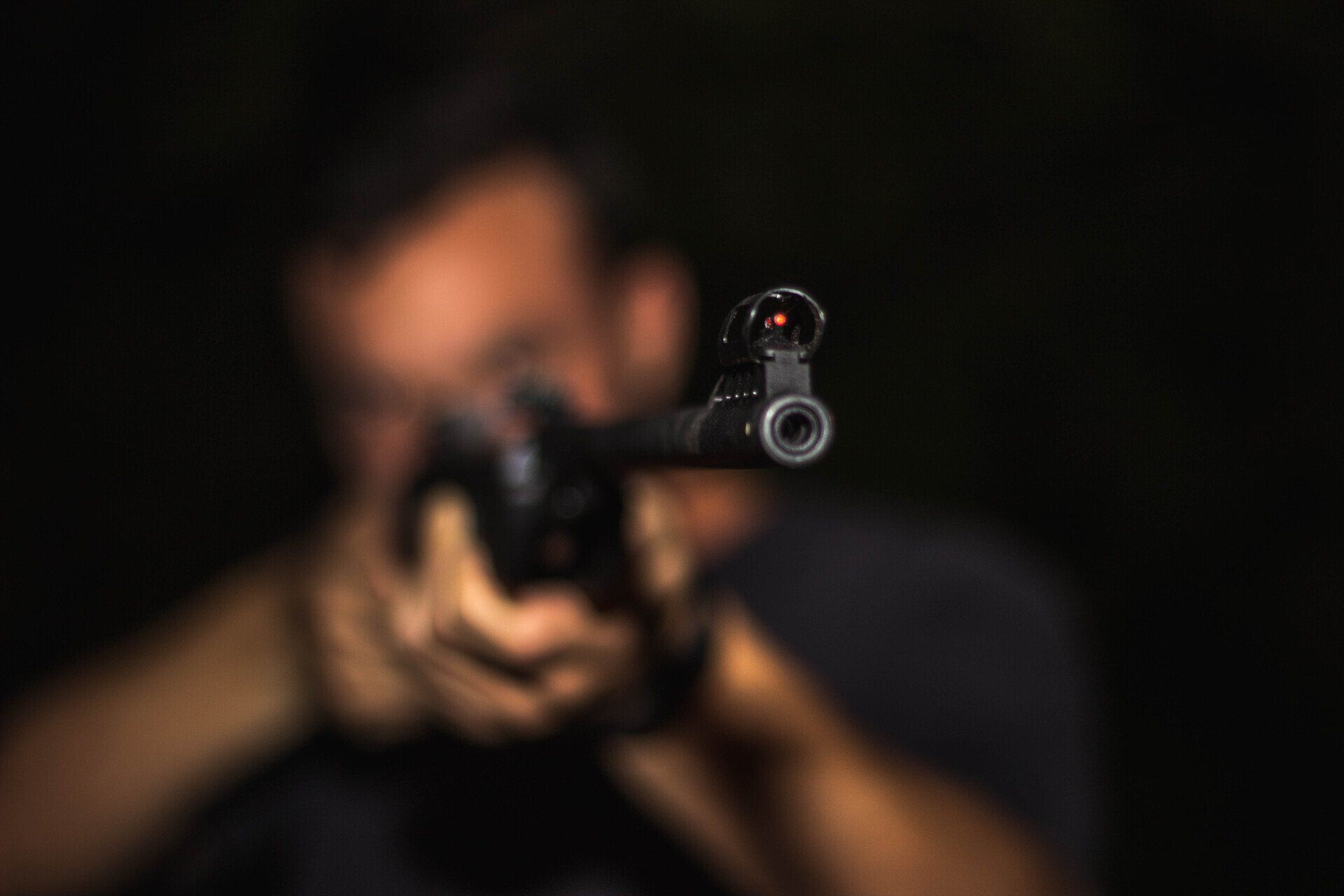 blurred image of man holding a rifle with barrel end in focus