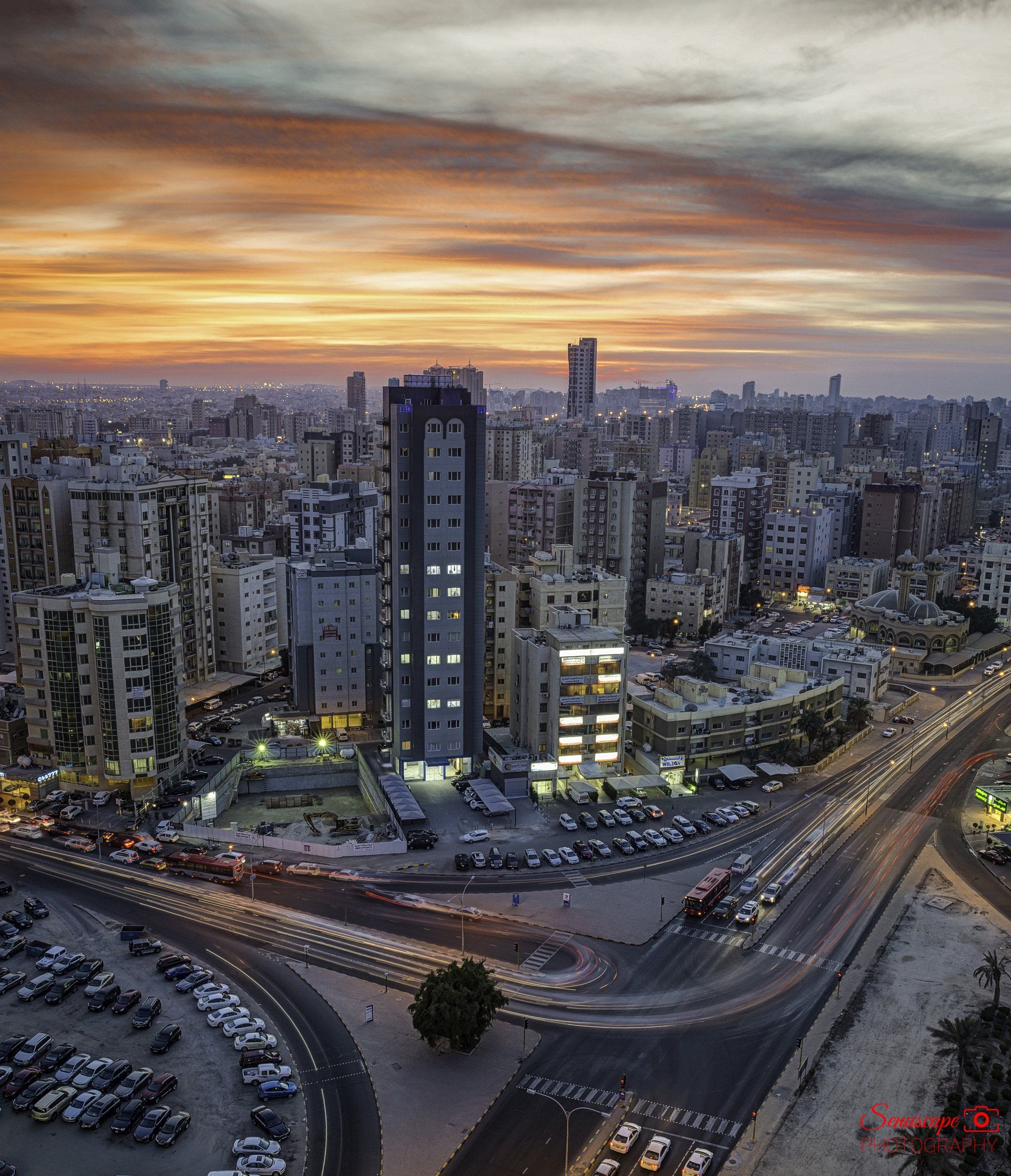 An aerial view of a city at sunset with a parking lot in the foreground.