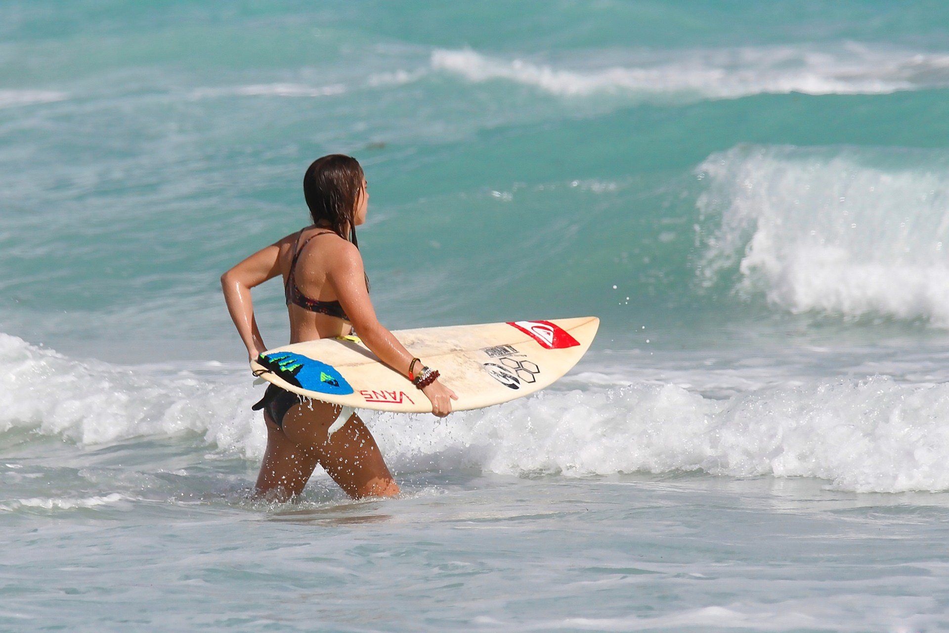 A woman in a bikini is carrying a surfboard in the ocean.