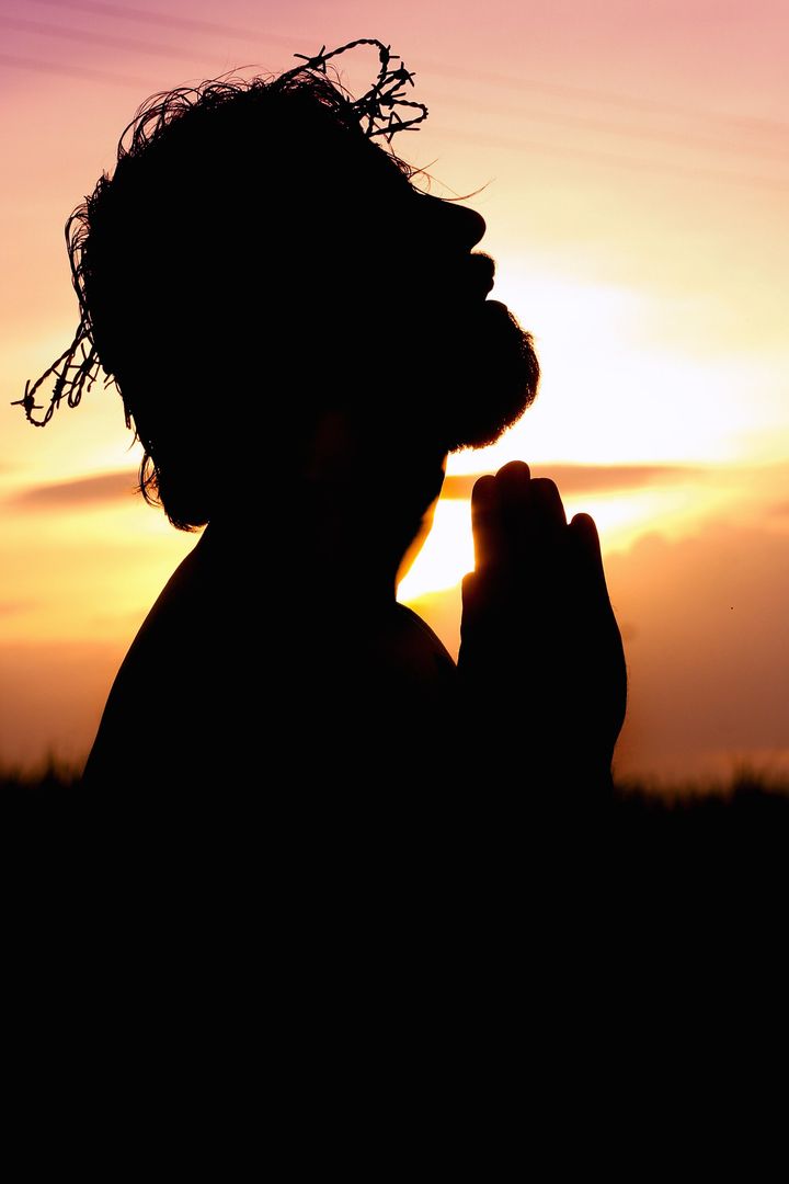 A silhouette of a man praying at sunset