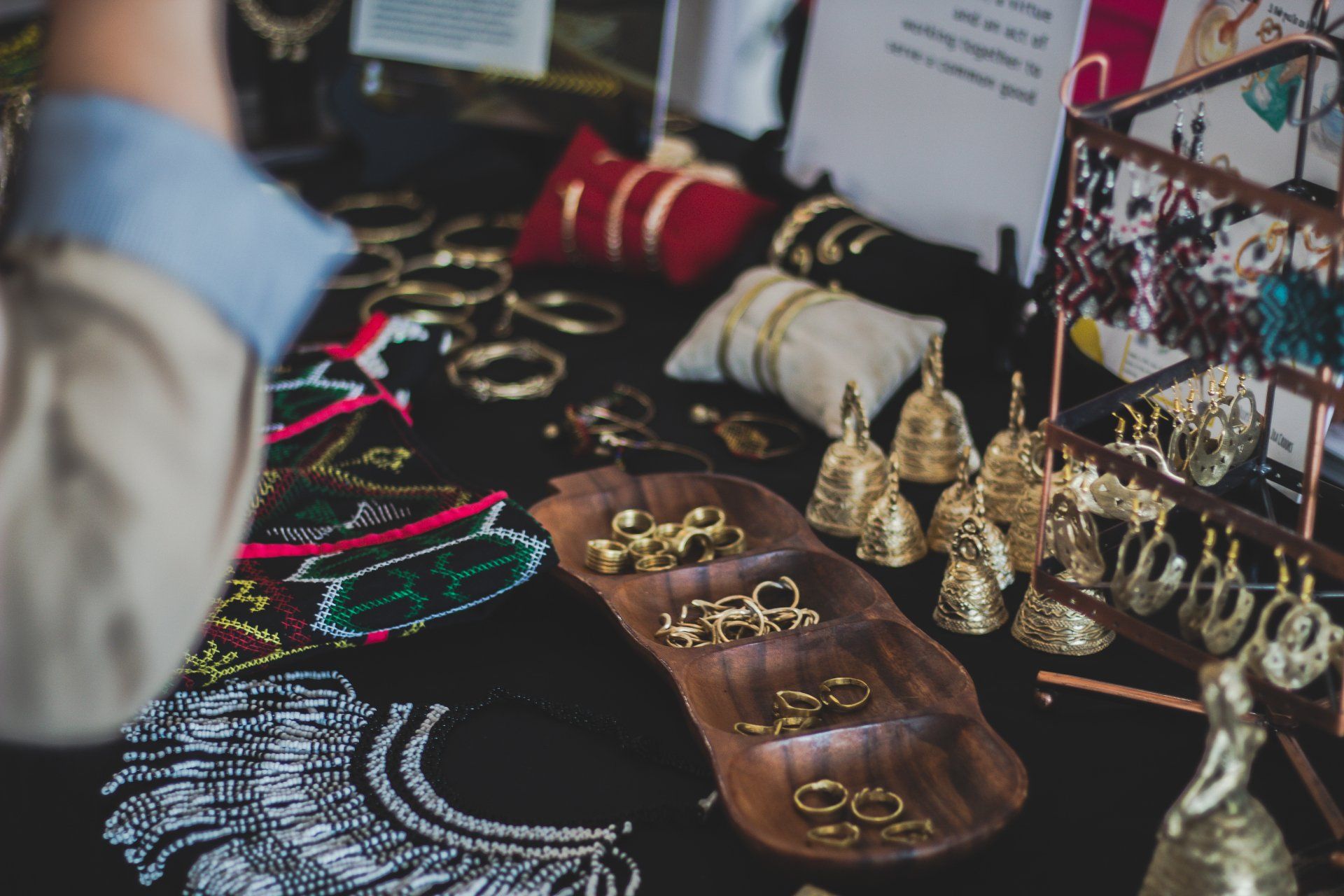 Exhibición de joyas sobre mesa negra con pulseras de oro, aretes y bandeja de madera.