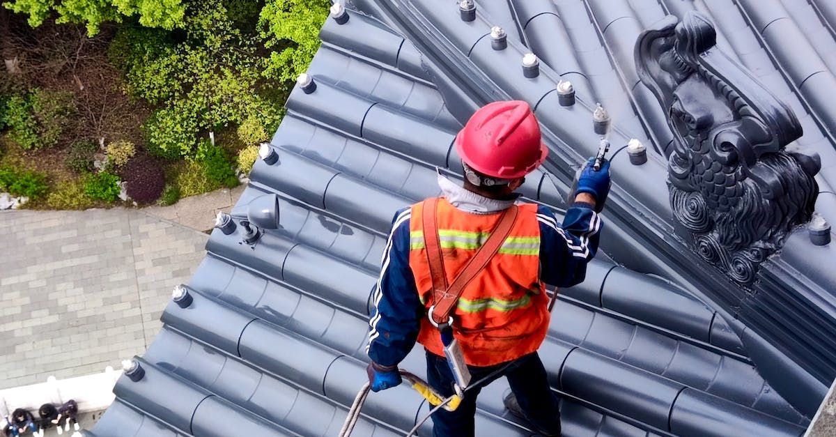 A man in an orange vest and hard hat is standing on a roof.