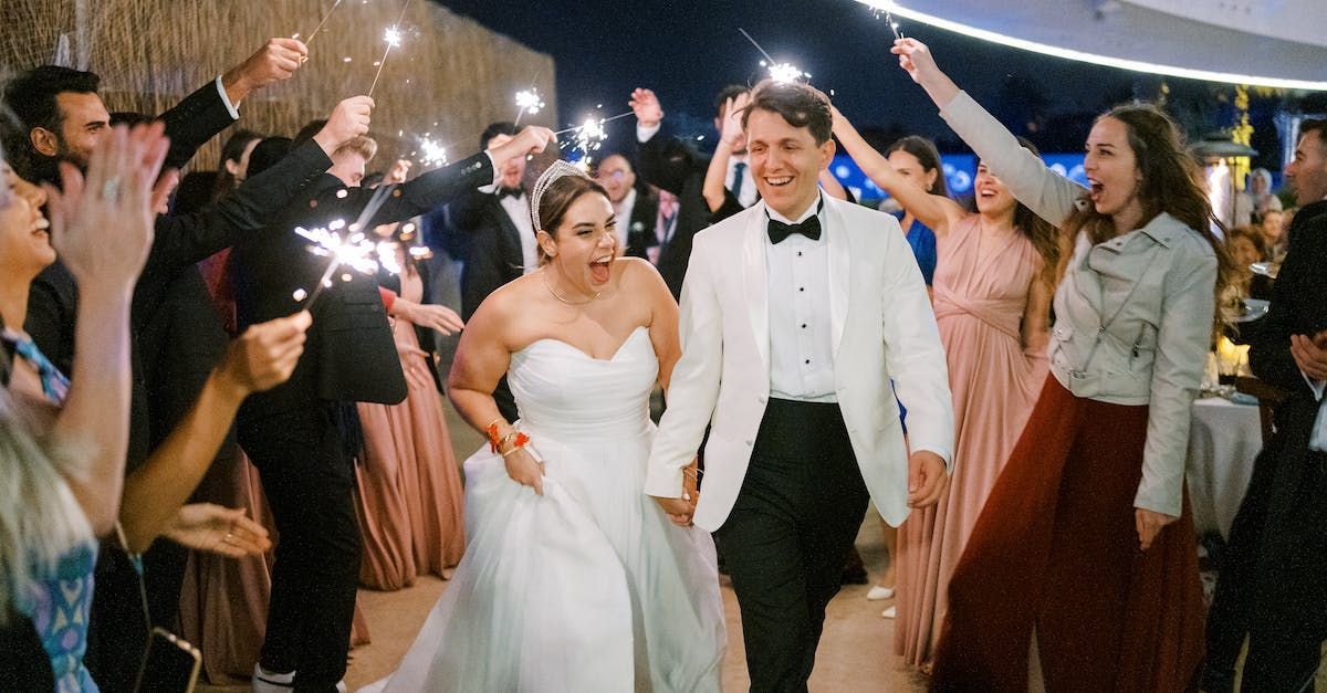 A bride and groom are walking through a crowd of people holding sparklers.