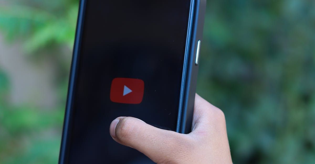 A person is holding a cell phone with a youtube icon on the screen.