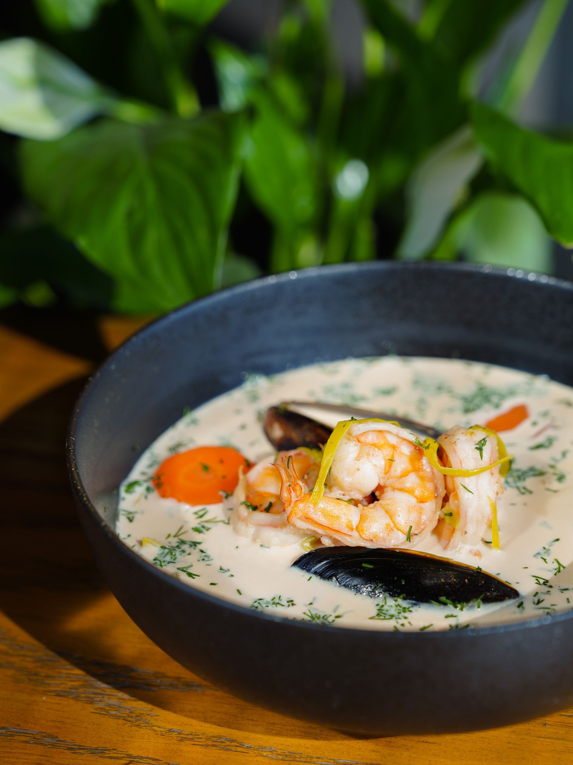Creamy seafood soup with shrimp, mussels, and vegetables in a black bowl.