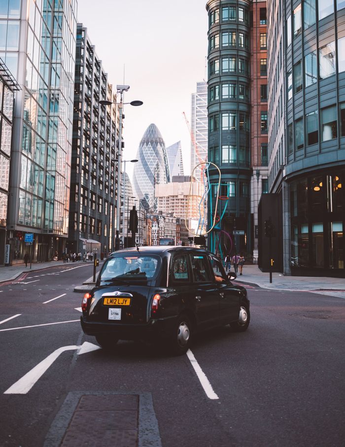 A black taxi cab is driving down a city street