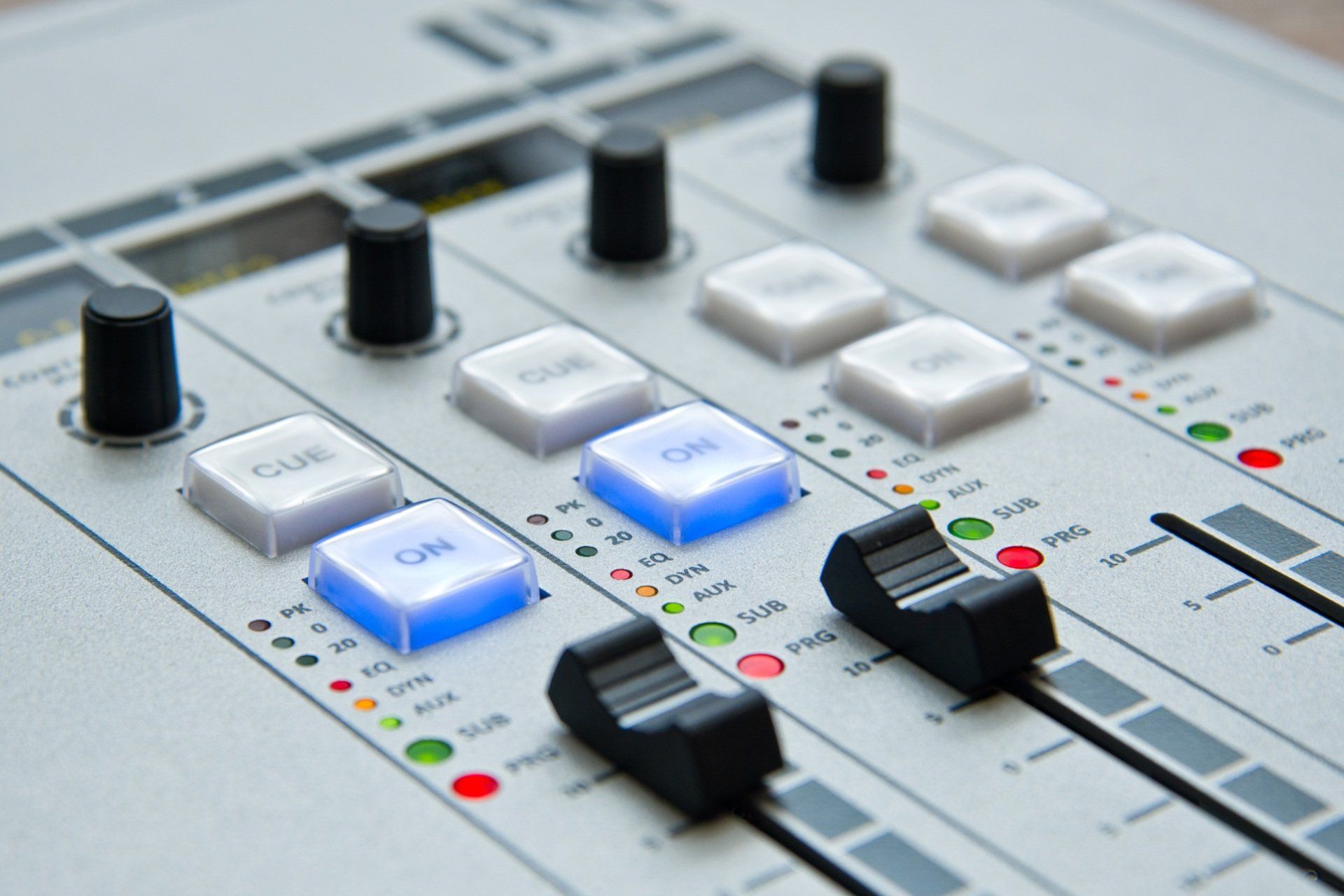 Close-up of a white audio mixing console with knobs, sliders, and glowing blue buttons