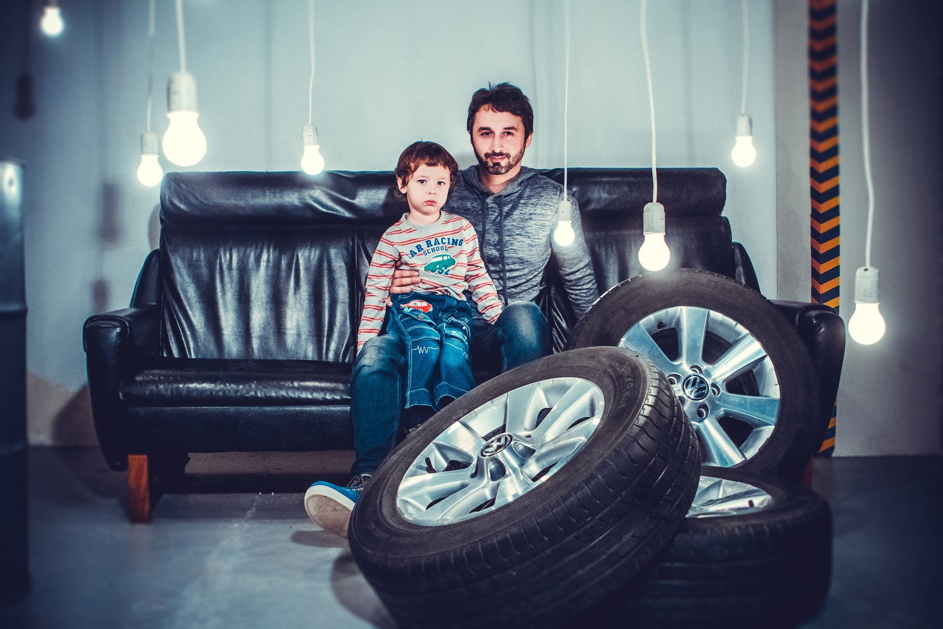 A man and a child are sitting on a couch next to tires.