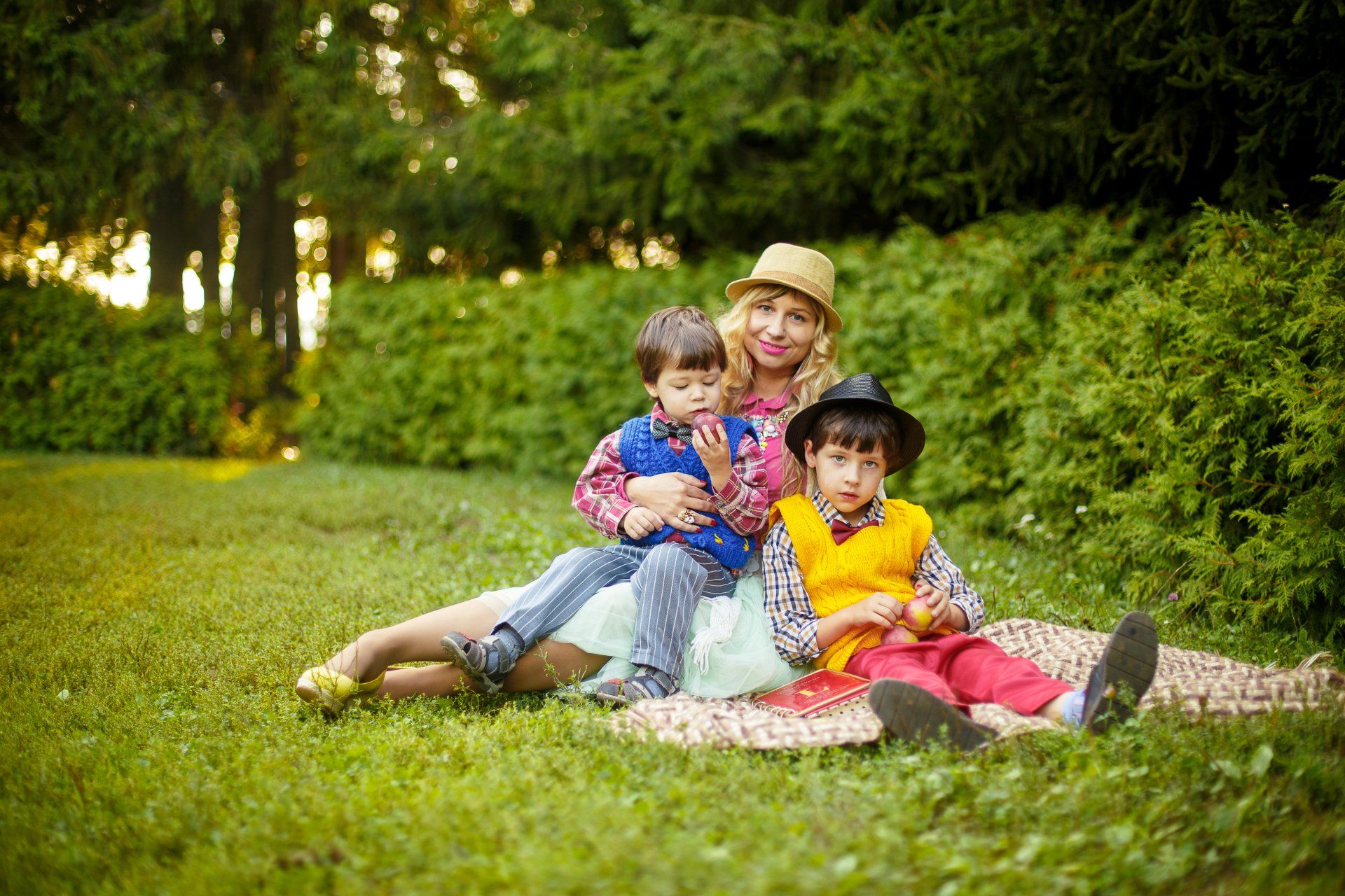 Woman in a hat holding two young boys in a field