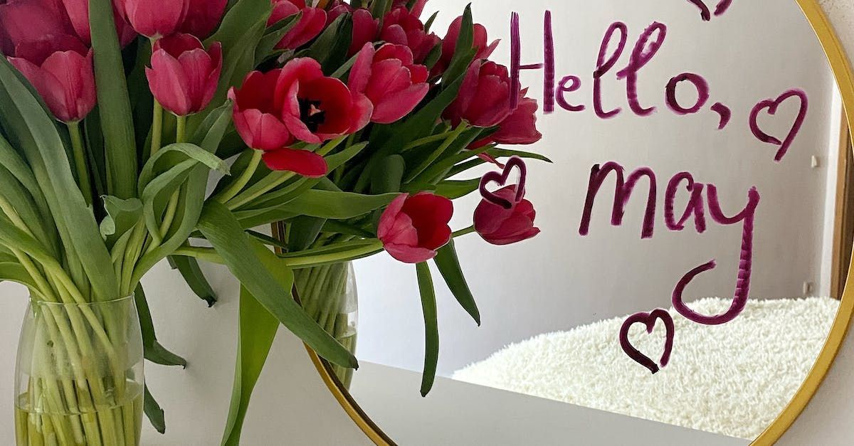 a vase of flowers sits next to a mirror that says hello may