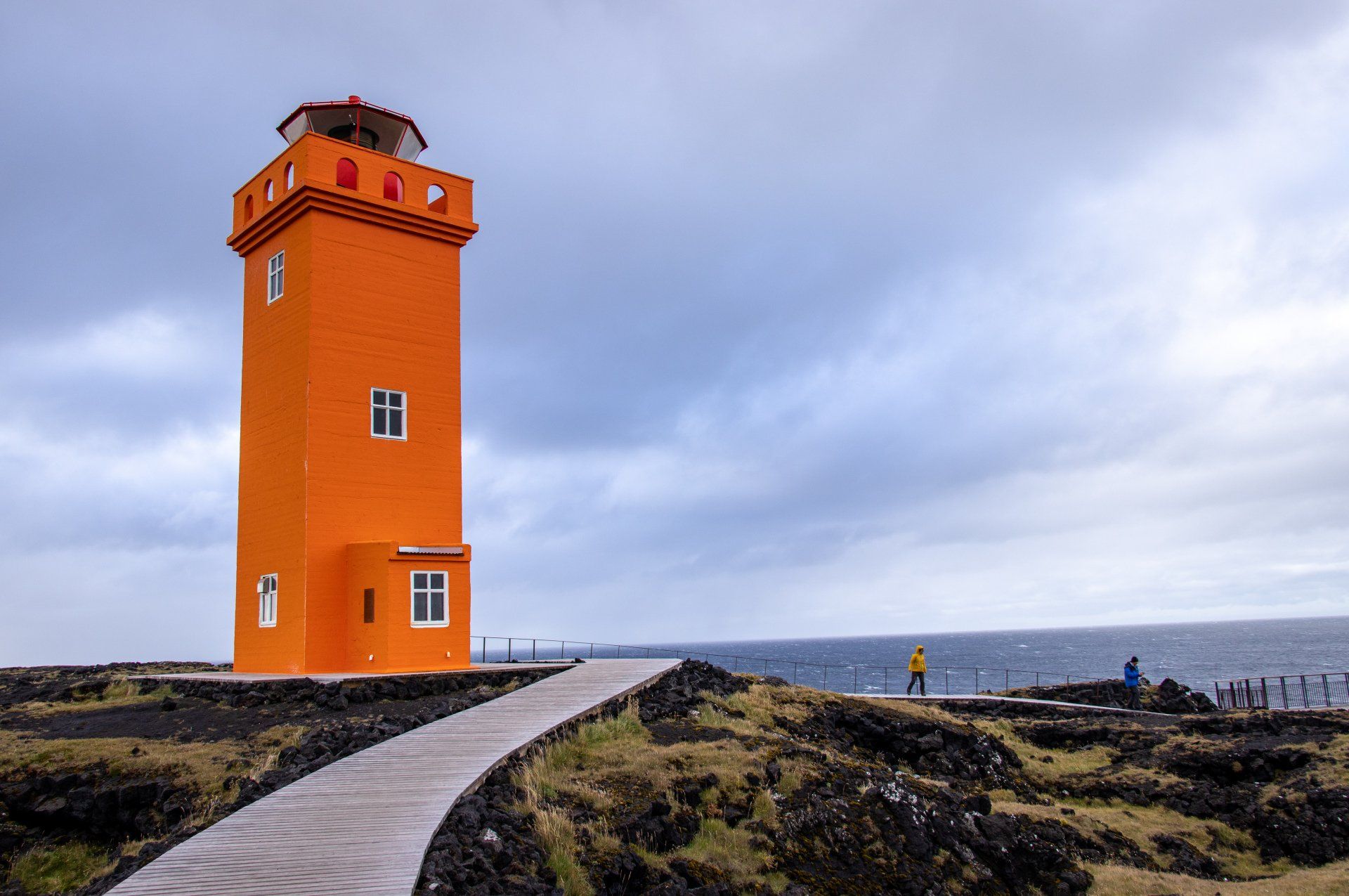 Et stort oransje fyr står på toppen av en høyde ved havet.