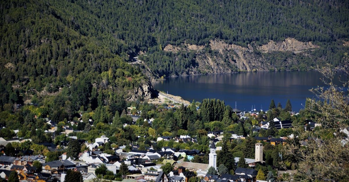 Lago de montaña sobre un pequeño pueblo, con un denso bosque y una costa rocosa al fondo.