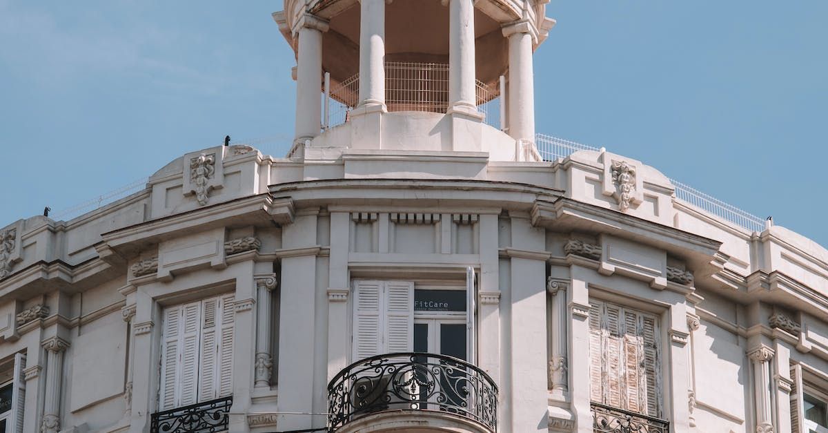 Ornate white building corner with dome, balcony, and blue sky.