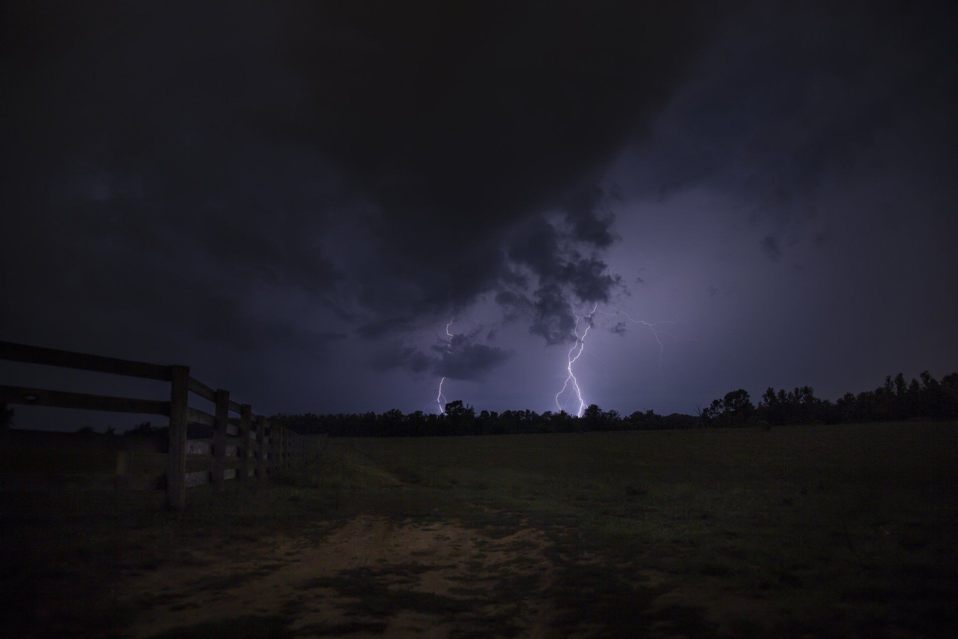 There is a lightning storm in the sky over a field at night.