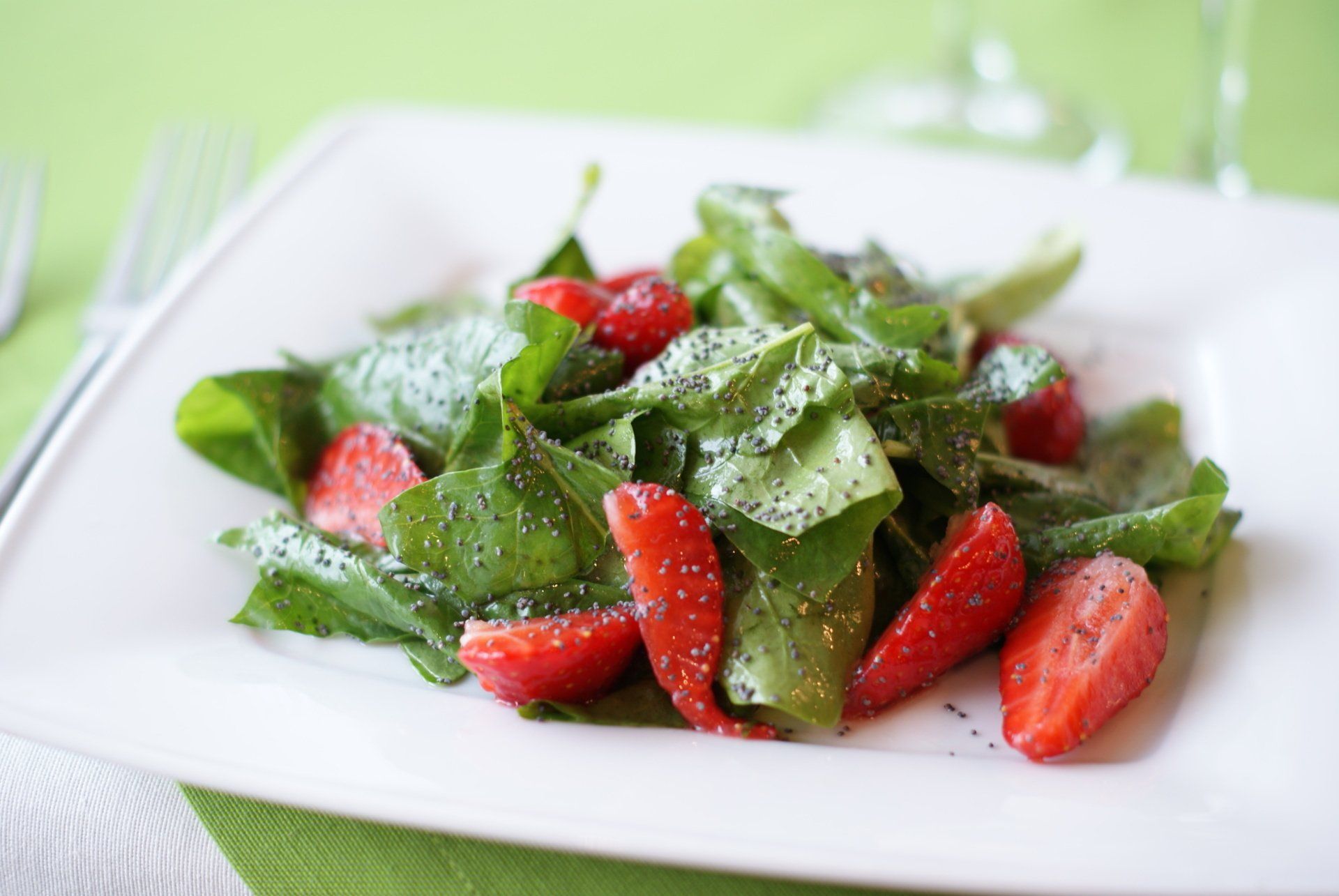 A white plate topped with strawberries and lettuce on a table.