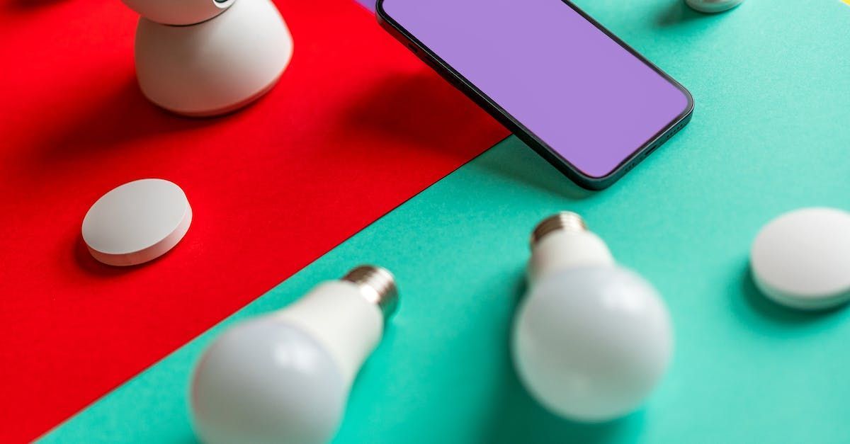 A cell phone , light bulbs , and a remote control are on a table.