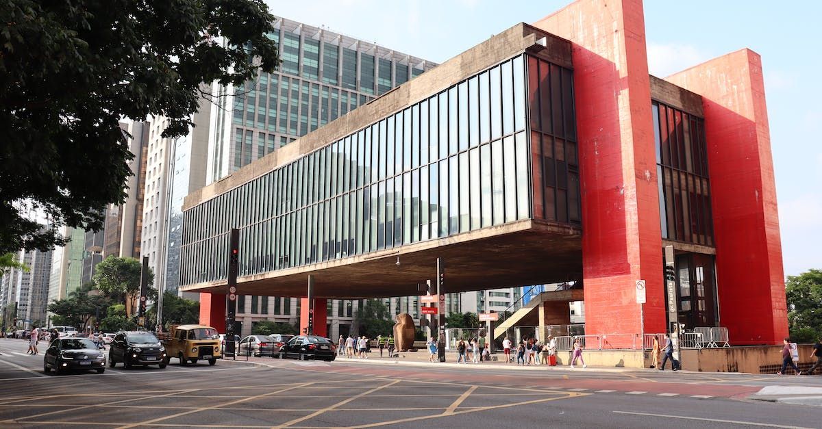 Modern building with red accents and glass facade on a city street, cars and pedestrians below
