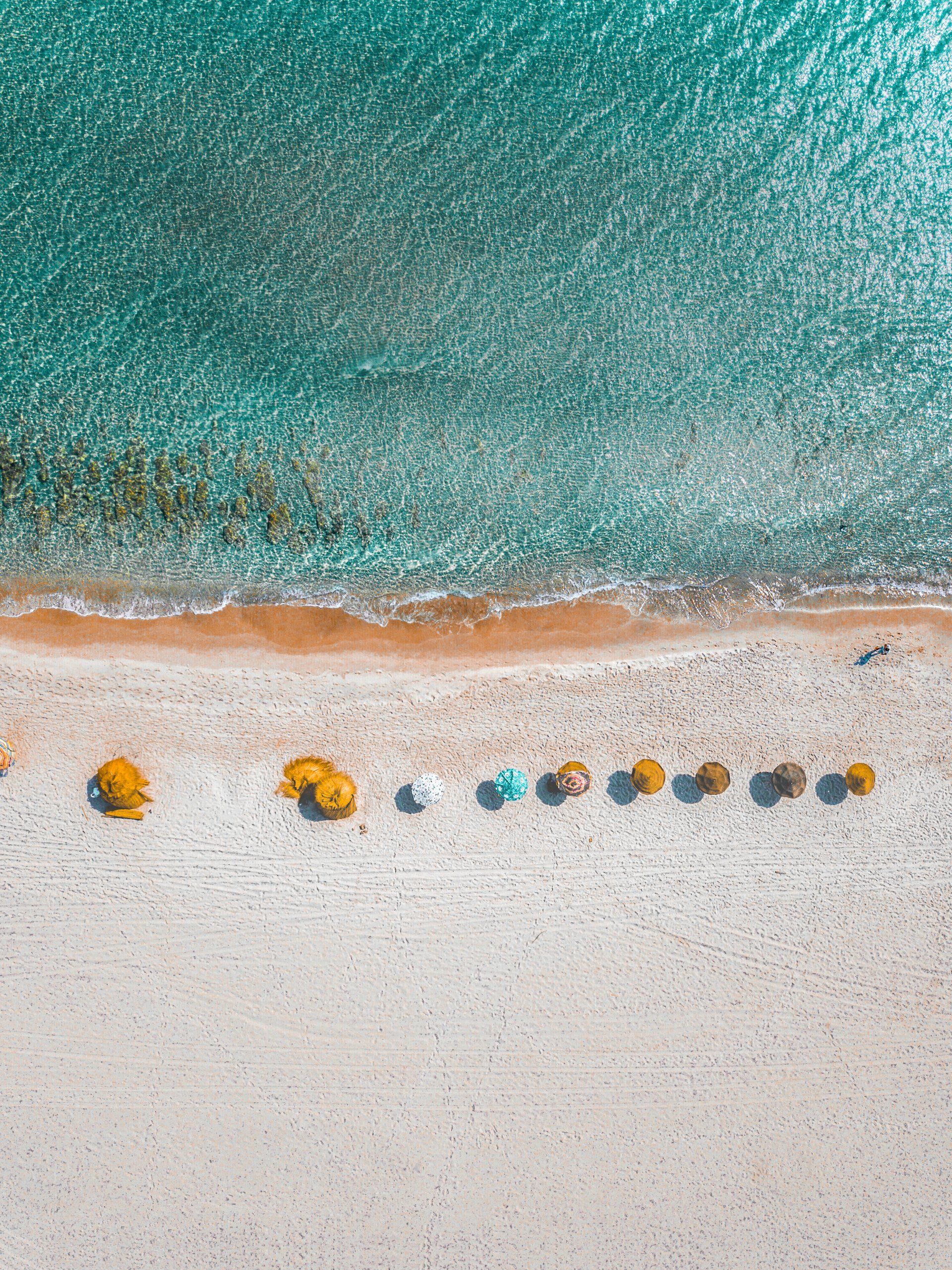 Uma vista aérea de uma praia com guarda-sóis e um corpo d'água.