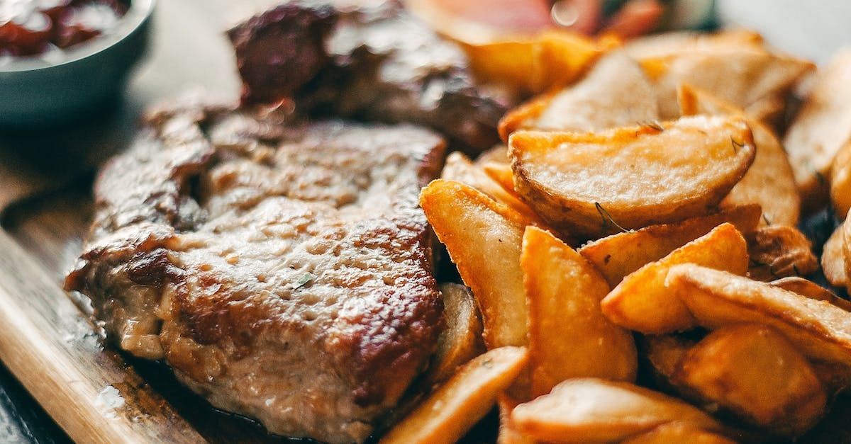 A steak and french fries on a wooden cutting board.