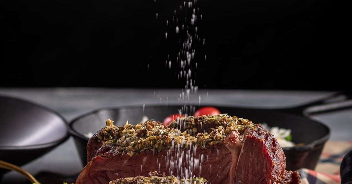 A piece of meat is being seasoned with salt and pepper.