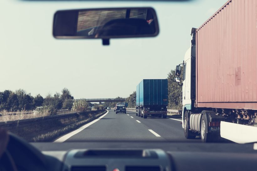 View from a car driving on a highway, with trucks in the adjacent lanes and trees in the background.