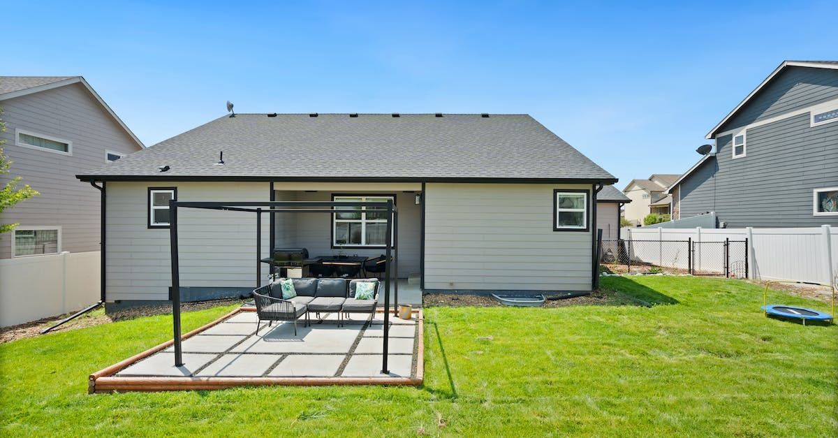 Backyard patio with table and chairs on a grassy lawn behind a single-story house