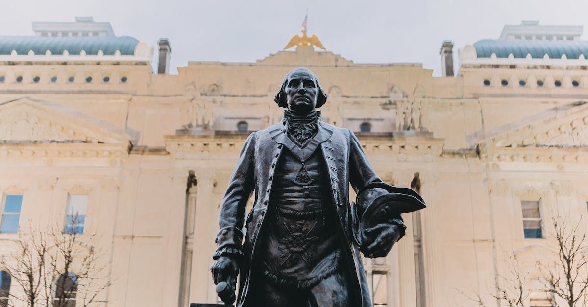 Bronze statue in front of a grand cream-colored building with a golden dome, viewed from below