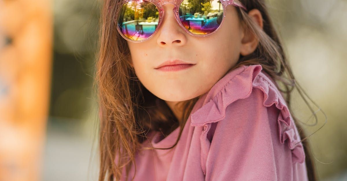 A little girl wearing sunglasses and a pink shirt is looking at the camera.