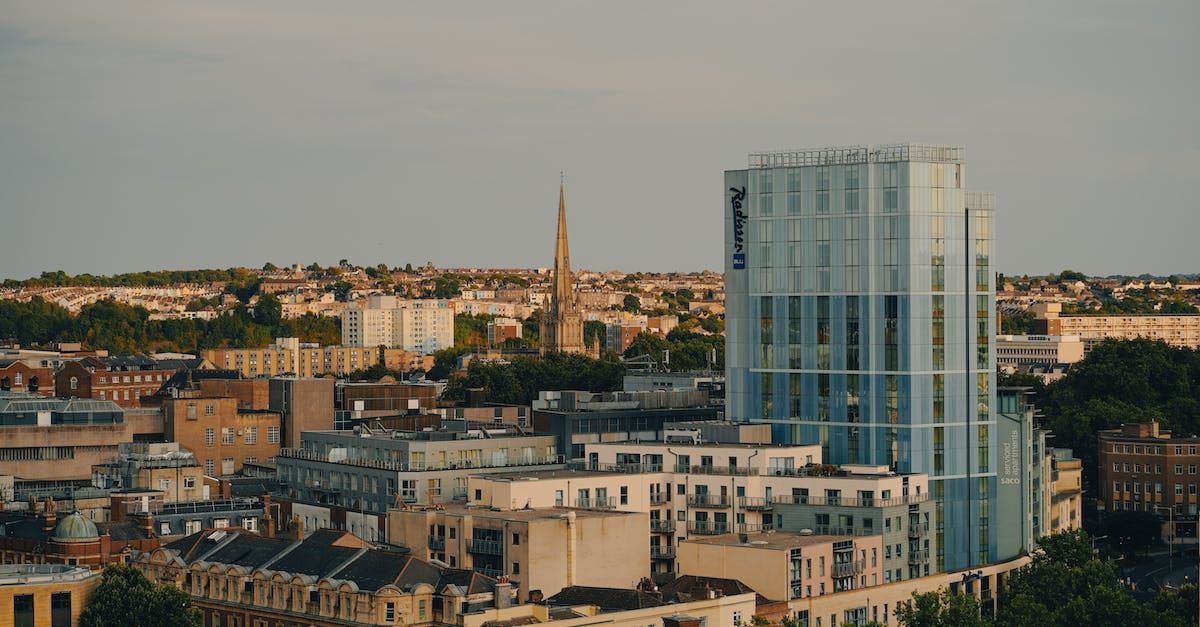 City skyline with a tall glass skyscraper and a distant church spire at sunset