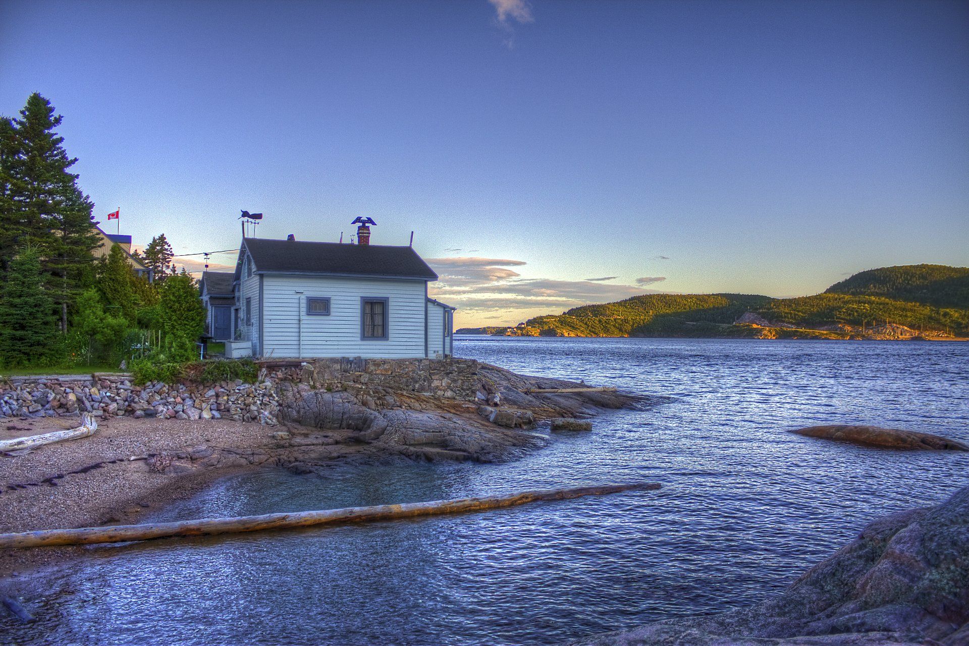 A small white house is sitting on the shore of a body of water.