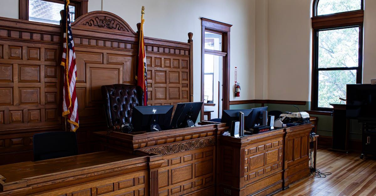 Wood-paneled courtroom with judge’s bench, black chairs, and large windows letting in daylight