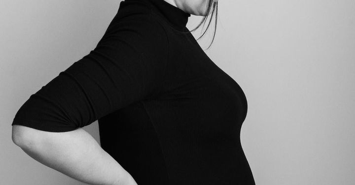 Side view of a person in a black top with hands on hips against a gray background
