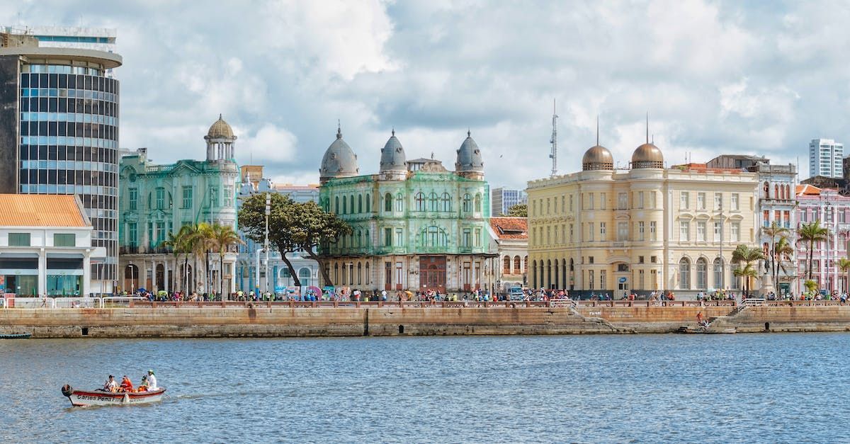 Waterfront city skyline with colorful historic buildings, a pier, and a small boat on the water