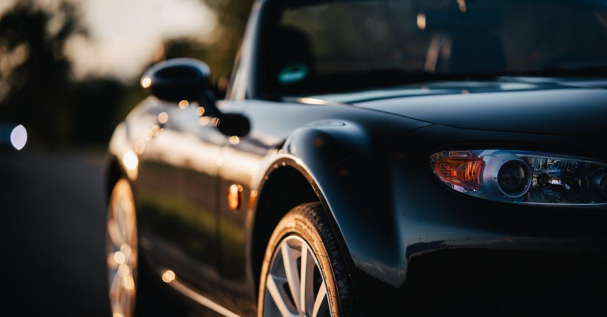 Black convertible car parked on a road at sunset, showcasing front fender, headlight, and wheel.