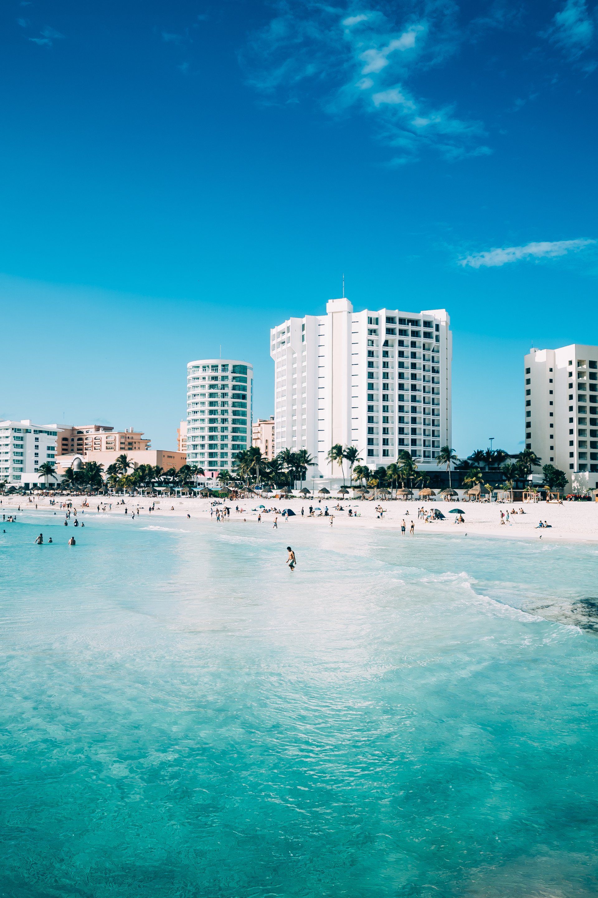 Turquoise water and white sand beach with several white high-rise buildings under a bright blue sky. Cancun,Mexico