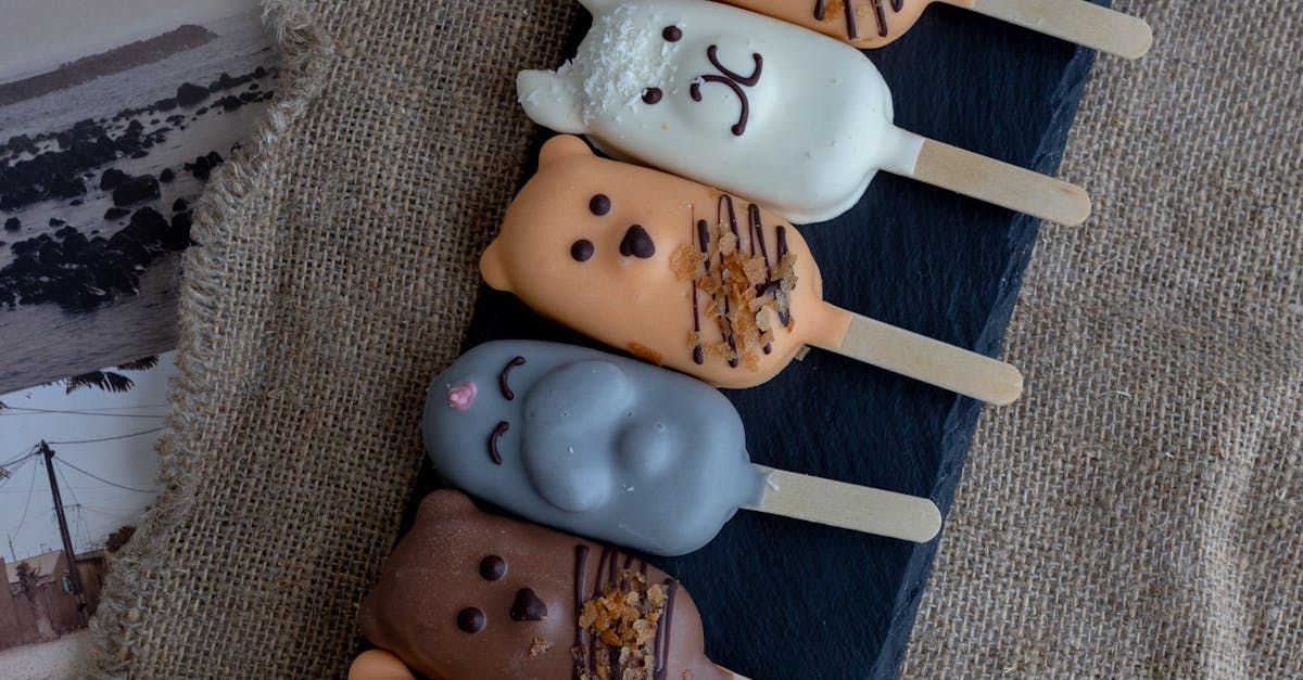 A row of five animal-shaped cake pops on sticks, resting on a dark slate board against a textured burlap background.