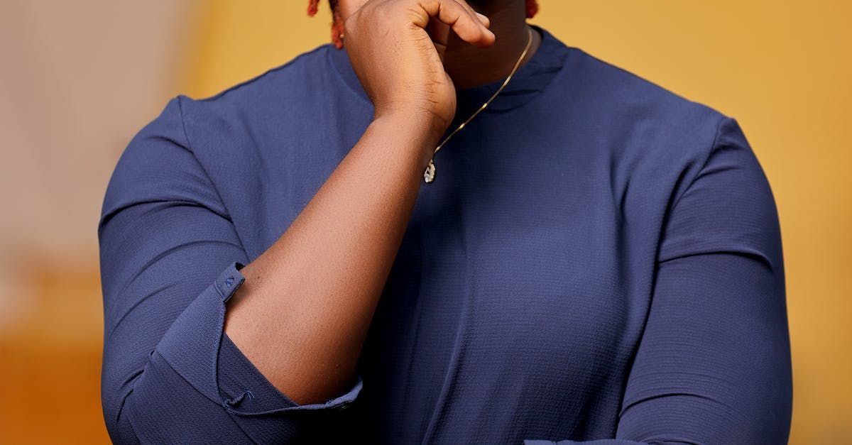 A man in a blue shirt is covering his mouth with his hand.
