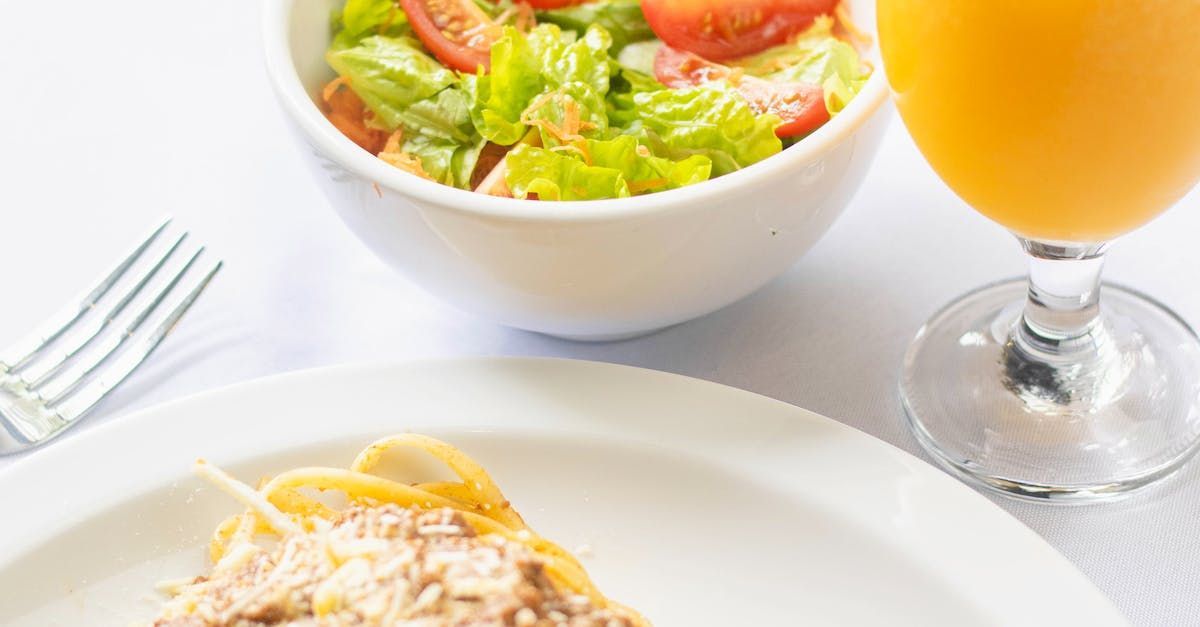 A plate of food next to a bowl of salad and a glass of orange juice.