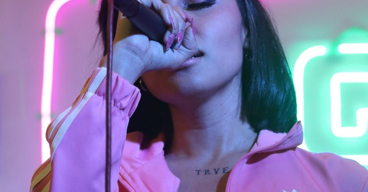 A woman in a pink jacket is singing into a microphone.