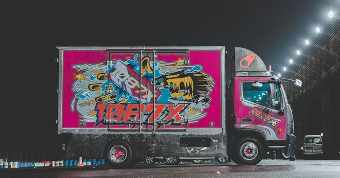 Pink and silver truck with colorful graffiti art on the side, parked at night.