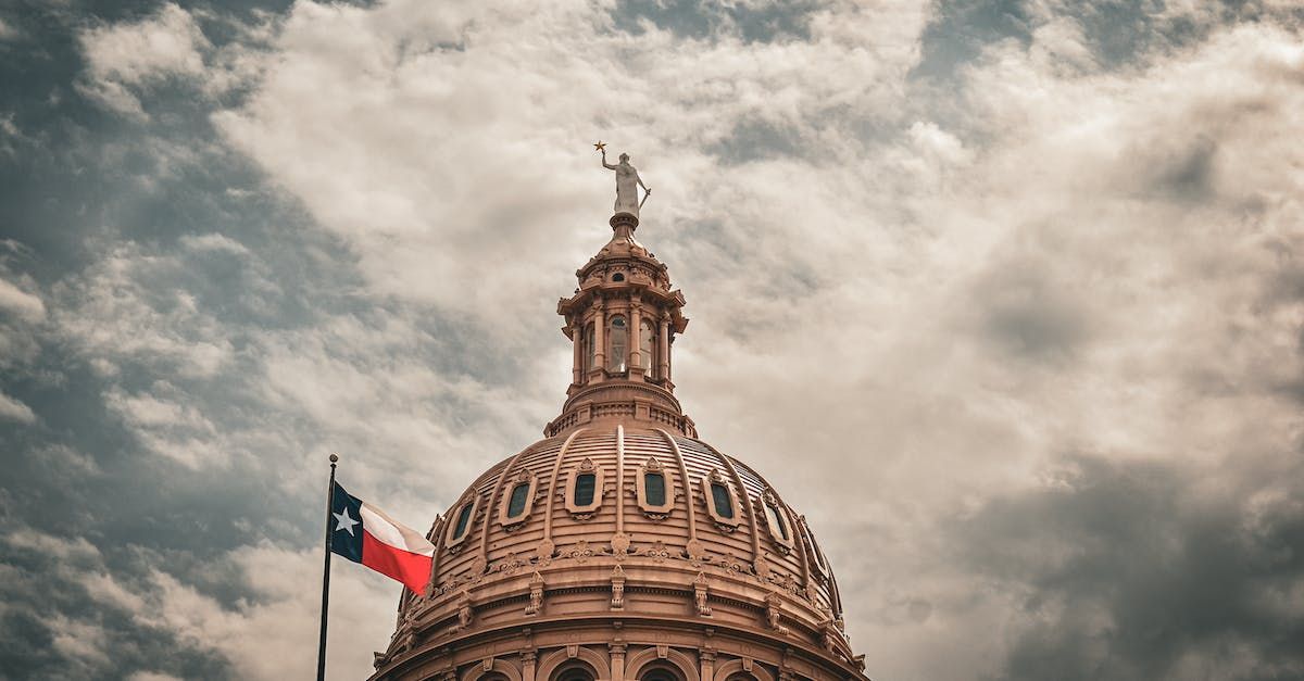 The dome of the texas capitol building with a texas flag flying in front of it.