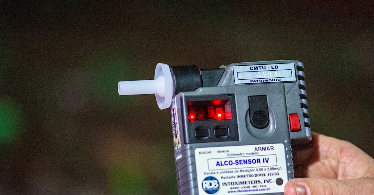 Hand-held breathalyzer with red lights illuminated, held against a blurred green background.